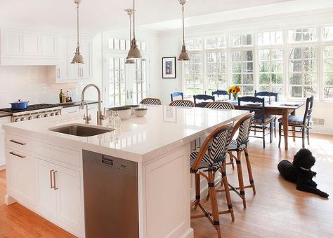 Fantastic kitchen features an expansive center island topped with white quartz framing a curved stainless steel sink and satin nickel gooseneck faucet placed next to a stainless steel dishwasher. Island With Sink And Dishwasher, White Kitchen Large Island, Kitchen Island With Sink And Dishwasher, Island With Sink, Sink And Dishwasher, Kitchen Islands Ideas With Seating, White Kitchen Cupboards, Kitchen Island With Sink, Sink In Island