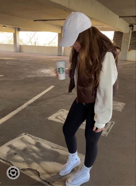 Girl in white baseball hat looking down at feet in parking garage. She is wearing white converse with black leggings, light yellow sweatshirt with brown cropped vest. Vest And Hat Outfits, Baseball Mom Outfits Casual, Outfits With Brown Vest, White Cap Outfits For Women, White Nike Hat Outfit, Brown Cropped Vest Outfit, Brown Baseball Cap Outfit, Beige Baseball Hat Outfit, White Baseball Hat Outfit