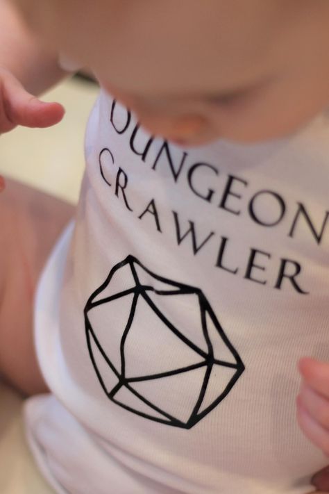 This one is perfect for the littlest members of your Dungeons and Dragons party. Your Dungeon Crawler can roll a D20 and will always succeed on their Charisma saving throws in this comfortable onesie. Nerdy baby clothes, dungeons and dragons baby clothes, d&d baby clothes. Dnd Gender Reveal, Nerdy Pregnancy Announcement, Nerdy Baby Announcement, Nerdy Nursery, Dungeons And Dragons Party, Nerdy Baby Clothes, Ash Baby, Nerd Baby, Dungeon Crawler