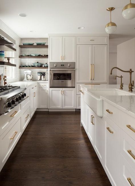 Gorgeous kitchen boasts white and gold pendants illuminating a white center island fitted with a farmhouse sink and antique brass hook and spout faucet. Off White Kitchen Cabinets With Dark Wood Floors, Kitchen With Brown Wood Floors, Small Kitchen Remodel Dark Floors, White Kitchen Dark Brown Floor, White Kitchen Cabinets With Brown Floor, Kitchen Brown Floor White Cabinets, White Kitchen With Dark Brown Floors, Kitchen Remodel Dark Wood Floors, White Kitchen Walnut Floors