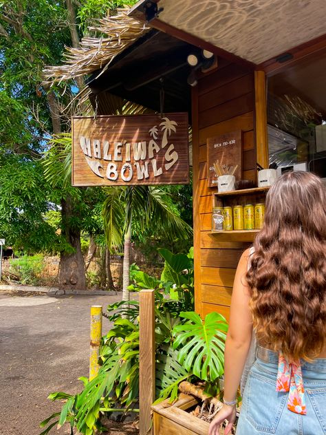 wooden Haleiwa Bowls shack surrounded by bright green leaves and a woman standing to the right ordering a smoothie North Shore Aesthetic, Hawaii College Aesthetic, College In Hawaii, Living In Hawaii Aesthetic, Oahu Aesthetic, Lihue Hawaii, University Of Hawaii At Manoa, North Shore Hawaii, Hawaii Aesthetic