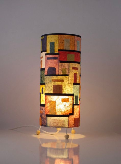 The Little Houses table lamp is handcrafted in Banana papers  38 cm tall by 15 cm diameter table/Desk lamp, when turned on, the lampshade allows light to pass through the screen, highlighting the patterns that really come to life, filling every corner with warmth, color and life, textures and shapes, style and trends, making it a true home.  Deisy Lamps Studio likes to bring colour, textures and life to any space, making a beautiful addition anywhere corner in a Home, Coffee Shop, Business Offic Eclectic Lighting Fixtures, Office Lighting Ideas, Paper Table Lamp, Banana Paper, Paper Lamp Shade, Decoration Studio, Contrast Texture, Diy Lampshade, Accent Lamps