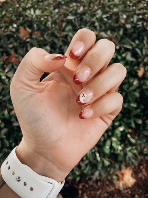 Hand with french manicure with a burnt orange color. One small ghost drawn on the ring finger. Neutral Halloween Nails Square, Ghost Oval Nails, Fall Time Nails Simple, Dip Nails For Halloween, Fall Nail Designs Ghost, Fall French Dip Nails, Fall Themed Short Nails, Ghost Dip Nails, Preppy Fall Nails Short