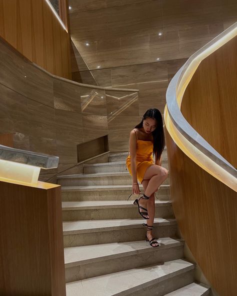 Young woman wear orange summer dress styled with black strappy block heels standing in a staircase in hotel lobby Poses In Heels And Dress, Poses On Stairs Instagram Dress, Tying Shoes Pose, Stairs Poses Instagram, Photo Ideas Stairs, Pictures On The Stairs, Poses With Heels, Orange Heels Outfit, Staircase Poses