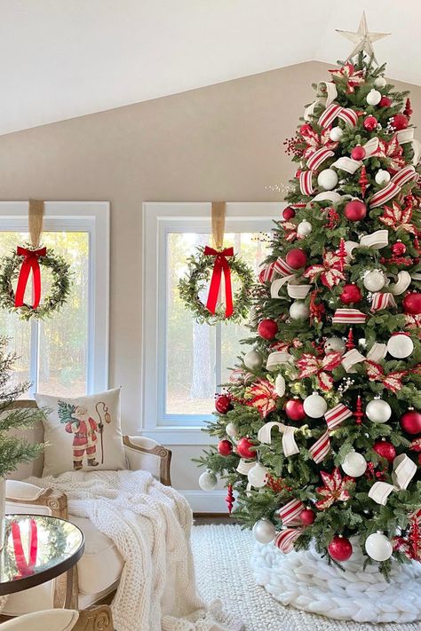 A Christmas tree decorated with red and white ornaments and ribbon, in front of windows with wreaths hanging in them with red bows. Red And White Christmas Tree Simple, Candy Cane Home Decor, Red Snd White Christmas Tree, Christmas Decoration Themes For Home, Christmas Tree Decorations Red And White, Christmas Decor Ideas Red And White, Classic Christmas Tree Ideas, Red Christmas Decor Ideas, Traditional Christmas Aesthetic