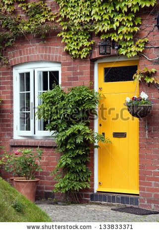 Yellow front door entrance and old style window of a red brick house or a cottage with hanging flower basket and green ivy. - stock photo Brick House Front Door Colors, Yellow Front Door, Red Brick House Exterior, Red Brick Exteriors, Orange Front Doors, Best Front Door Colors, Exterior Door Colors, Yellow Front Doors, Best Front Doors