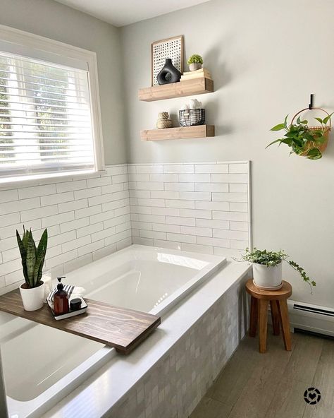 White framed window provides this neutral bathroom with natural light. White tile surrounds an alcove bathtub with wood accents arranged within this space. Bathroom floating shelves are affixed to the wall. White Bathrooms With Wood Accents, Bathtub Wall Shelf, Floating Shelves Above Tub, Tub Wall Ideas, Shelves Over Tub, Bathtub Wall Decor, Bathroom 2024, Built In Bathtub, Bathroom Wood