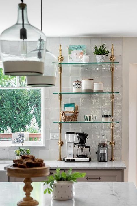 Kitchen features a glass and brass plumbing French style shelf on gray glazed wall tiles and a cake plate on a marble topped kitchen island illuminated by vintage glass lanterns. French Bistro Shelves Kitchen, Open Shelving Decor Ideas, Shelving Decor Ideas, Kitchen Open Shelving Decor, Open Shelving Decor, French Bistro Kitchen, Kitchen Open Shelving, Bistro Shelving, Shelving Decor