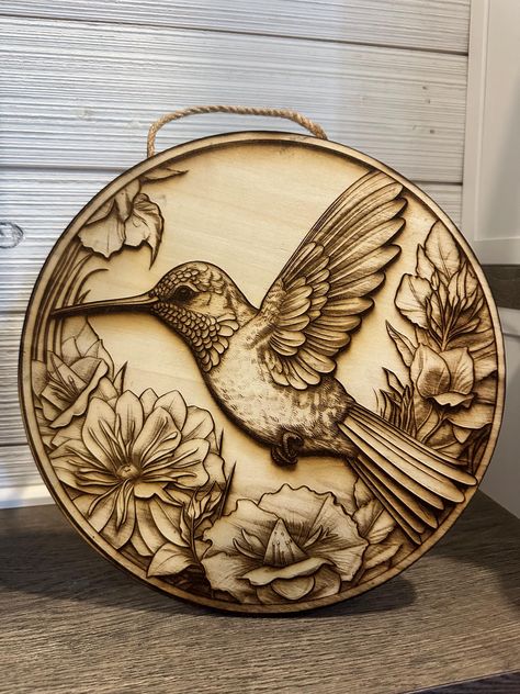 Laser engraved 3D illusion wooden plaque features picturesque humming bird. Plaque is a high quality craft plywood and is sealed using a satin finish clear coat. Plaque is approximately 12" wide Ideal for indoor décor, decoratively placing on a shelf or displaying on a wall using the included jute rope. **Please note: Items are made on different pieces of wood and given the nature of natural materials used, there may be slight differences in wood spots, wood grains, etc. Wood Carving Wall Art, Bird Wall Hanging, Wood Burning Patterns Stencil, Wood Burning Stencils, Wood Art Diy, Wood Burn Designs, Illusion 3d, Woodburning Projects, Pyrography Art