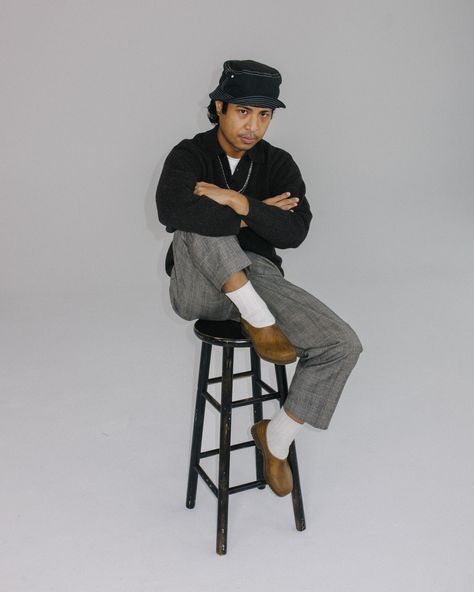 Man wearing bucket hat, white socks, clogs, and gray pants. He is sitting on a stool, arms crossed with one leg up and one leg down. Gardenheir Clogs Outfit, Gardenheir Clogs, Garden Clogs Outfit, Gardana Clog, Swedish Clogs Outfit, Styling Clogs, Clog Outfit, Stylish Walking Shoes, Clogs Outfit