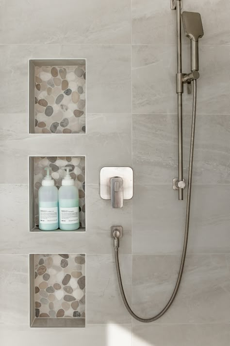 Your shower niche is the perfect opportunity to create some visual interest. Here we used a smooth river stone tile to draw the eye but also to create some material repetition as the tile was also used for the shower floor as well. Design by Kierstin Smyth Design. Photo Credit: Darren Lebeuf #edmontonbathroomrenovation #edmontoninteriordesign #tripleshowerniche Stone Shower Niche, Shower Niche Large Tile, Shower Inset Shelves, Shampoo Niches In Showers, Niche In Shower Wall, Shower Wall Niche Ideas, Vertical Shower Niche, Shelves In Shower, Shower Niche Placement