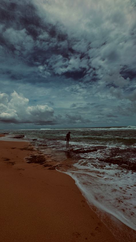 This image captures a serene and moody beach scene under a dramatic, cloud-filled sky. The sandy shore extends into the distance, with gentle waves washing over the wet sand. A lone figure stands near the edge of the water, gazing out towards the horizon, giving the image a sense of solitude and contemplation. The dark, brooding clouds above create a stark contrast with the lighter tones of the beach, enhancing the overall atmospheric feel of the scene. The image exudes a sense of quiet reflection, perhaps just before or after a storm, with the vast ocean stretching out under the ominous sky. Turtles, Moody Beach, Vast Ocean, Wet Sand, A Lone, Beach Scene, Beach Scenes, A Storm, The Horizon