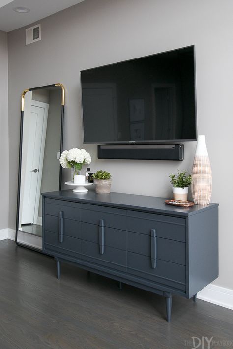 Love this gray bedroom dresser with the TV mounted above it. Plus then you can use the top of it to display pretty accessories. Love the large vase and wood tray from HomeGoods. Don't forget to add some height to the dresser with a cake stand! You can then display perfume and candles on top. (Sponsored Pin). Bedroom Dresser With Tv, Dresser Decor Bedroom, Tv Mounted, Dresser With Tv, Tv In Bedroom, Bedroom Dresser, Gray Bedroom, Trendy Bedroom, Dresser Decor