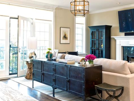 This neutral condo living room features an antique sideboard that serves as a console table behind an off-white sofa. A chandelier with a metal geometric pattern provides light for the space, and a dark glass-front cabinet provides storage and display space. Behind Sofa, Table Behind Couch, Condo Living Room, Behind Couch, Storage Inspiration, Industrial Livingroom, Traditional Interior Design, Couch Decor, Trendy Living Rooms