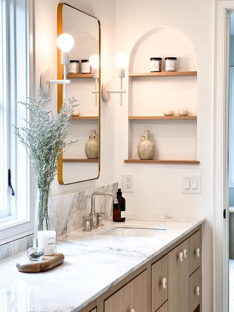 This bathroom has all the most beautiful design features! From the marble countertop and backsplash, the oak vanity and unique knobs, to the arched niche with shelves built into the wall, it truly is impressive!    New Construction | Home Trends 2024 | Home Design | Minnesota Home Trends Built In Tiled Shelves Bathroom, Built In Niche Bathroom, Arch Niche Bathroom, Arched Niche In Wall Bathroom, Marble Bathroom Shelves, Built Ins In Bathroom, Bathroom Vanity Niche, Niche With Shelves, Vanity Niche