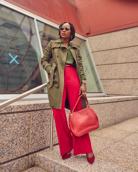 A black woman in a color-blocked outfit. She is wearing red pants and an army green shirt and trench coat with a red Louis Vuitton handbag. Red And Army Green Outfits, Army Green Shirt Outfit, Green Pants Outfit Work, Poncho Outfit Fall, Army Green Trench Coat, Olive Green Trench Coat, Army Green Outfit, Olive Green Pants Outfit, Olive Trench Coat