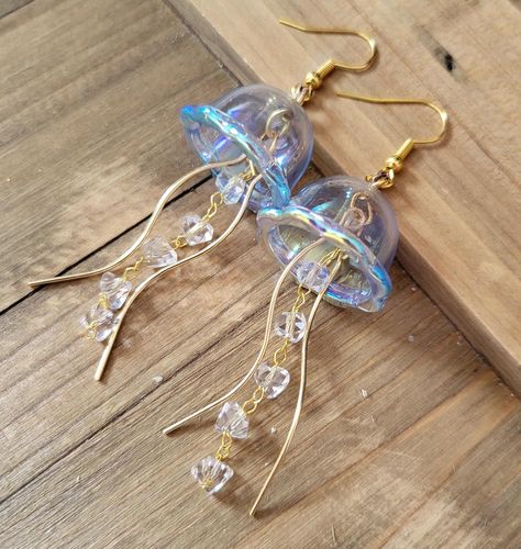 18k gold plated stainless steel handmade earrings of light blue aura jellyfish. These Jellyfish are made from dainty blue iridescent acrylic domes, glass crystal studded chain, and gold wisp tendrils.  The difference between these earrings and my popular Jellyfish earrings are the domes- unlike my green, teal, pink, and purple ones, these domes are made from a hard plastic so they are less fragile, and can be coated in the rainbow iridescent aura that is color shift depending on lighting and angle.  Please note that these earrings jingle similarly to my glass Jellyfish earrings that dangle. They are not too loud, and make a really cute jingly sound as you move. If you are sensitive to earrings making sound as you wear, then these earrings may not be for you. Thank you for your understandin