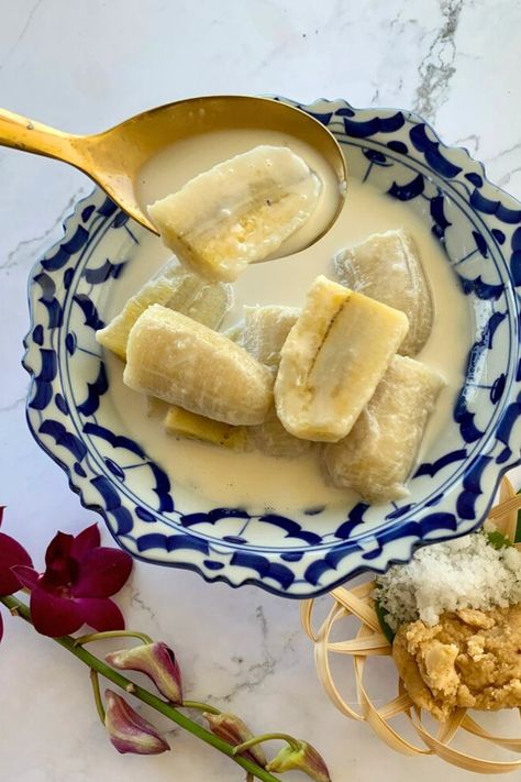 Bananas in coconut milk in a blue-white dish with a golden spoon holding a piece of banana.