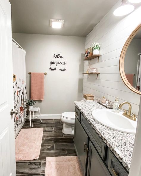 Gray bathroom wall and white shiplap unite in this elaborately decorated bathroom. Wood shelves occupy the wall joined by black lettering. Pink bathroom dГ©cor including mats and towel add a touch of color to dark flooring and vanity. Pink Black And White Bathroom Decor, Grey And Blush Bathroom Ideas, Blush Color Bathroom Ideas, Gray Pink Bathroom, Blush And Gray Bathroom, Pink Gray Bathroom Ideas, Pink Gray And White Bathroom Ideas, Blush Pink Bathroom Ideas, Pink And Gray Half Bathroom