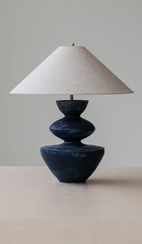 Handmade ceramic lamp base with conical oatmeal linen shade. Choice of satin 'anthracite' black (pictured), translucent 'stone' matte white (pictured), washy 'lapis' blue (pictured), crackle terra sigillata 'terrasig' white, matte 'ivy' green, matte 'chestnut' brown or metallic 'bronze' base finish. Approximately 23" tall including shade, 12" diameter ceramic base at widest point, 20" diameter shade. 10' 6" cotton cord with Pierre Krings prong plug. Takes (1) G16 shape, 60W max. incandescent bul Danny Kaplan Lamp, Handmade Ceramic Lamp, Clay Luminaries, Danny Kaplan, Clay Lamp, Blue Ceramic Lamp, Terra Sigillata, Ceramic Lamp Base, Ceramic Lamps