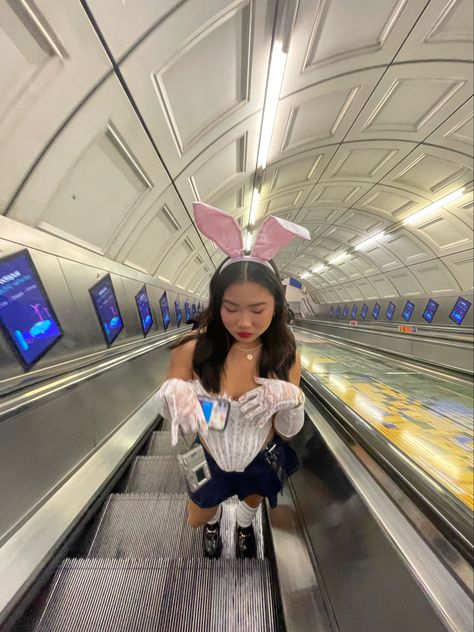 girl on escalator is white rabbit costume from Alice in wonderland. White corset, denim skirt, lace gloves, and white rabbit ears White Rabbit Costume Alice In Wonderland Party, Alice In Wonderland And White Rabbit, White Rabbit Alice In Wonderland Costume Women, Alice And Wonderland Bunny Costume, Alice And Wonderland Rabbit Costume, The White Rabbit Halloween Costume, Alice And The Wonderland Costumes, White Bunny Alice In Wonderland Costume, White Bunny Costume Alice In Wonderland