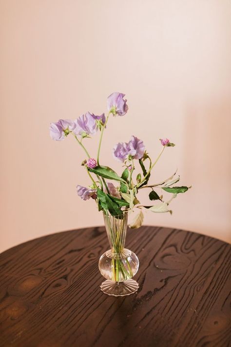 This image features a wooden cocktail table at a wedding cocktail hour. The table has a geometric bud vase filled with lavender sweet pea florals and greenery Lavender Sweet Pea, Green Wedding Centerpieces, Red Flower Arrangements, Decor Palette, Bud Vases Flowers, Jp Morgan, Green Centerpieces, Gallery Photography, Photography Location