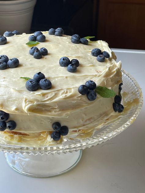 a photo of a round yellow cake with whipped buttercream icing garnished with blueberries and mint on a glass cake stand Lemon Blueberry Cake Aesthetic, Lemon And Blueberry Cake Decoration, Pretty Cakes Simple, White Cake With Blueberries, Homemade Birthday Cake For Boyfriend, Blueberry Cake Aesthetic, Homemade Birthday Cake Decorating, Berry Cake Decoration, January Birthday Cake