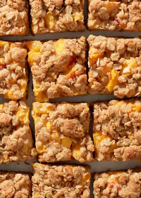 A close up of peach crumble bars lined up on a parchment paper background. Peach Oatmeal Breakfast Bars, Peach Breakfast Bars, Gluten Free Peach Crumble Bars, Mini Peach Crumble, Peach Oat Bars, Peach Oat Crumble, Peach Oatmeal Bars, Peach Crumb Bars, Peach Bars