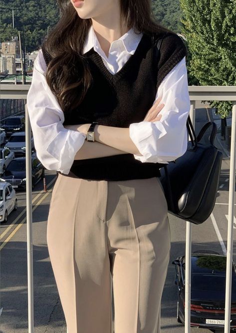 Achieve a timeless and polished look with this classic layered outfit featuring a black knit sweater vest over a crisp white button-down blouse. Paired with tailored beige trousers, casual and sophisticated. Whether for work or a coffee date, this look delivers effortless elegance. Accessorized with a sleek black leather bag and minimalist watch.

#LayeredLook #ClassicOutfit #BusinessCasual #MinimalistFashion #EffortlessChic #OOTD #styleguide Sweater Vest Formal Outfit, Retro Vest Outfit, Vest Aesthetic Outfit, Korean Classy Outfits, Korean Work Outfit, Casual Work Outfits Women, Simple Casual Outfits, Stylish Work Attire, Business Casual Outfits For Work