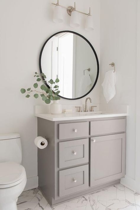 Round black mirror above a gray single washstand fitted with a white quartz countertop and a satin nickel faucet in a transitional bathroom. Cabinet Repainting, Modern Master Suite, Makeover Kamar Mandi, Nickel Faucet, Dining Room Renovation, Desert Boho, Transitional Bathroom, Hall Bathroom, White Oak Floors