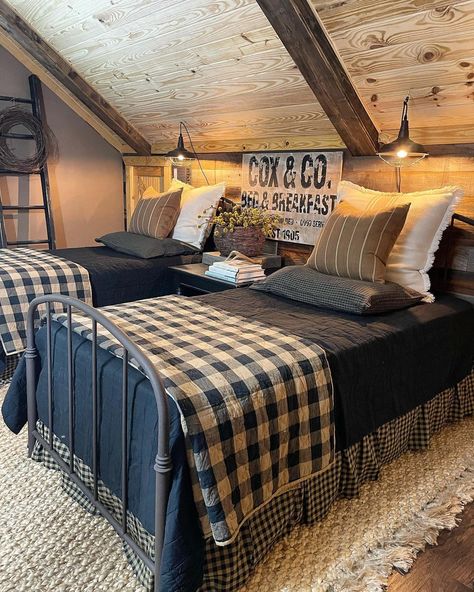 Two blue metal twin beds are pushed against a wood shiplap bedroom wall. Blue, beige, and white pillows are strewn at the head of the bed. Blue bedspreads cover the beds underneath folded blue and white checkered quilts laid at the foot of the bed. The checkered bed skirt hangs down to the white rug sitting on the warm wood floor. Outdoorsy Guest Bedroom, Navy Blue Country Bedroom, Bedding For Cabin, Twin Beds Guest Room Farmhouse, Quilt Bedspread Ideas, Blue Buffalo Check Bedroom, Masculine Farmhouse Bedroom, Blue Plaid Bedroom, Blue Country Bedroom