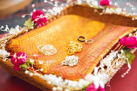 The manthrakodi basket: A decorated basket which includes the manthrakodi (wedding sari that the groom drapes over the bride), thali and thread/chain (form of a necklace that the groom ties around the bride’s neck to symbolize their marriage union), wedding rings and rosaries. Lots of significant wedding details in one container! 📸: ILS Weddings Manthrakodi Basket, Stage Designs, Thread Chains, Wedding Sari, Groom Ties, Stage Design, The Groom, Wedding Trends, Unique Wedding