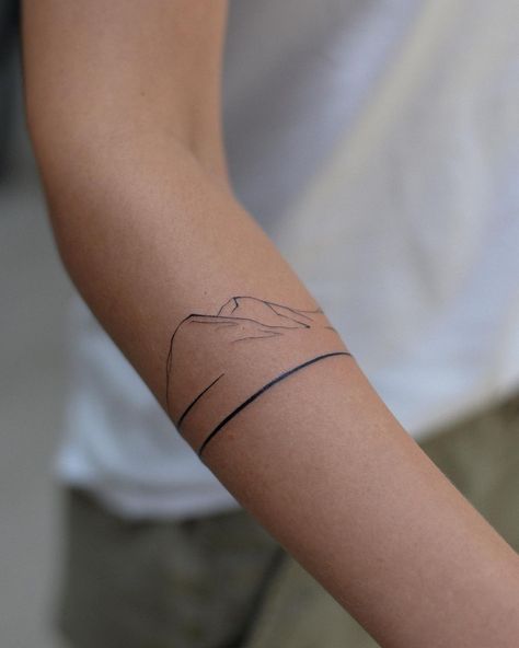 20 Mountain Tattoo Ideas That Prove The Power Of Simplicity Arm Band Mountain Tattoo, Mountains Around Arm Tattoo, Mountain Back Of Arm Tattoo, Wrap Around The Wrist Tattoos, Mountain Tattoo Arm Band, Mountain Wrap Tattoo, Simple Wrap Around Tattoo, Arm Mountain Tattoo, Fineline Mountain Tattoo