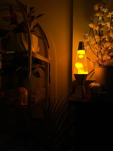 White lava lamp off-center to the right with orange lava flowing at night in the dark. Lamp is on a mantle to the left of a white floral display. There is a decorated golden arched shelf to the left of the mantle. Dark vignette creating a moody orange and black photograph. Lava Lamp Decoration, Bedroom Lava Lamp, Ambient Lighting Studio Apartment, Orange Candle Aesthetic, Warm Lighting Lamp, Lava Lamp Living Room, Lava Lamp Room Aesthetic, Lava Lamp Decor, Lava Lamp Aesthetic Room