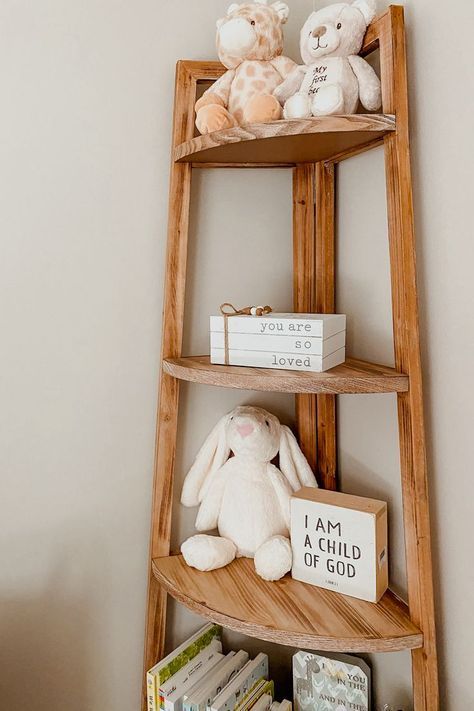 A picture of a natural wood corner shelf with gender neutral nursery decor including neutral stuffed animals and wooden knick knacks. Standing Shelf In Nursery, Nursery Standing Shelf, Wood Accent Nursery, Simple Cozy Nursery, White And Wood Nursery Ideas, Gender Neutral Nursery Simple, Gender Neutral Small Nursery, Gender Neutral Nursery Small Space, Nursery Gender Neutral Themes