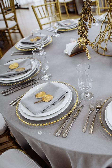 Gray polyester linens from CV Linens offer a simple yet sophisticated way to dress up your table. When paired with gray napkins, gold beaded charger plates and gold center pieces, you will create a classic base for an elegant tablescape. The subtle color is a perfect color to compliment other colors allowing you to decorate for any event theme. gray wedding colors, gray table setting wedding, gray table decor, gray wedding theme, silver gray wedding theme Gray Napkins Wedding Table Settings, Grey Table Cloth Setting, Gray Wedding Table Setting, Gold And Silver Place Setting, Silver Gray Wedding Theme, Gray And Gold Table Setting, Grey And Gold Wedding Decor, Gray Plates Table Settings, Silver Gold Wedding Theme