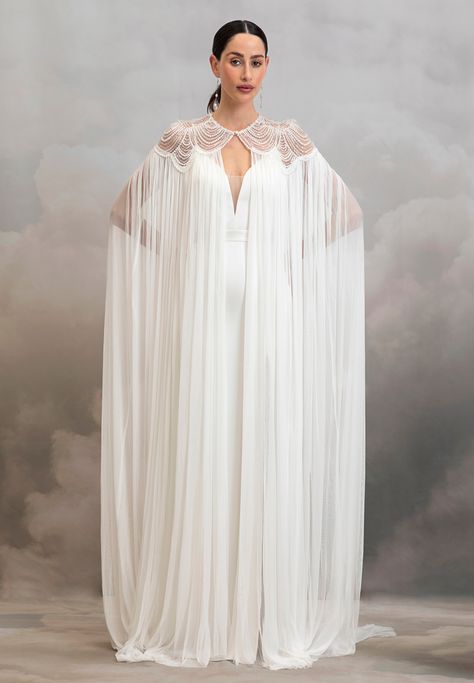 Add instant glamour to your bridal look with the dramatic Aster Cape. Pearl scalloped tulle embrace the neckline and shoulders of this whimsical cape before it drapes down in the softest 100% silk tulle. We suggest pairing this piece with a classic wedding gown or a topper and silky bridal trouser set to instantly elev Classic Wedding Gown, Wedding Cloak, Catherine Deane, Fantasy Outfits, Cape Gown, Cape Wedding Dress, Bridal Jumpsuit, Wedding Cape, Bridal Cape