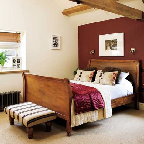 Wooden sleigh bed with striped footstool, beamed ceilings and red feature wall. Red Bedroom Walls, Red Feature Wall, Red Apartment, Feature Wall Bedroom, Red Bedroom, Warm Bedroom, Accent Wall Bedroom, Red Wall, Bedroom Red