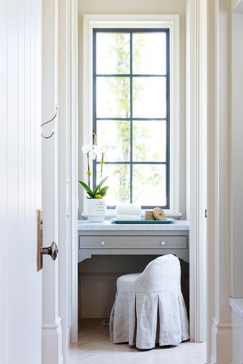 Gray built-in makeup vanity nook with a low back skirted stool under a black vertical window with lovely natural warm glowing light. Nook In Bathroom, Vanity Nook In Bathroom, Makeup Vanity Nook, Vanity In Front Of Window, Closet Makeup Vanity, Built In Makeup Vanity, Vanity Nook, Vanity In Bedroom, Built In Vanity