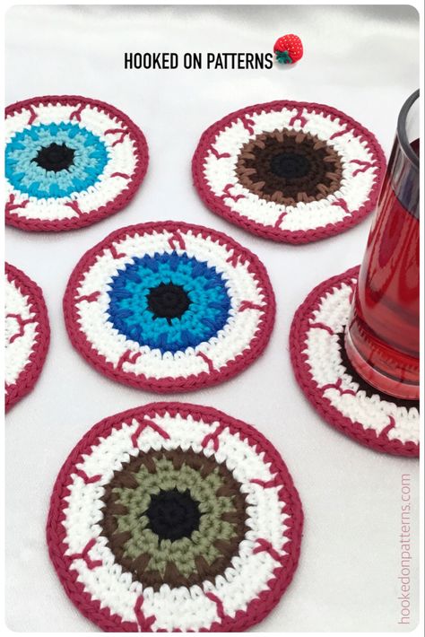 crocheted eyeball coasters in different eye colours Crochet Halloween Door Decor, Crochet Eyeball Sweater Pattern, Crochet Spiderweb Coaster Pattern, Crochet Eyeball Pattern Free, Halloween Decor Crochet, Crochet Halloween Coasters, Spooky Crochet Patterns Free, Creepy Crochet Pattern Free, Eye Crochet Pattern