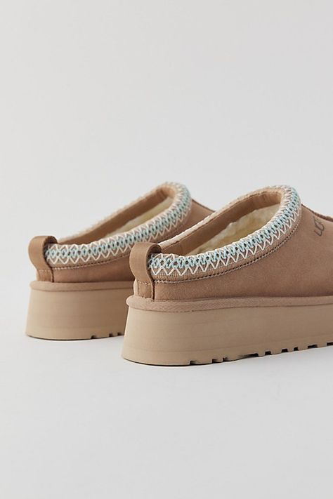 A maximalist take on the timeless Tasman, the Tazz refreshes the familiar silhouette with a platform sole for boosted cushioning and style. Crafted from the same rich suede as the original, it's lined in signature UGGplush™ wool blend for a slipper-like feel indoors or out. UGG® Tasman braid (70% recycled polyester, 30% rayon) and heat-embossed logo. Content + Care Suede, UGGplush™ (80% upcycled wool, 20% Lyocell), EVA Spot clean Imported Size + Fit True to size Platform height: 1.5" | UGG Tazz Slipper in Sand, Women's at Urban Outfitters Indoor Shoes Woman, Ugg Slippers For Kids, Tan Shoes Women, Costal Granddaughter Shoes, Ugh Platform Slippers, Cute Shoes For Winter, Ugg Slippers Kids, Uggs Slippers Platform, Shoes Slip On