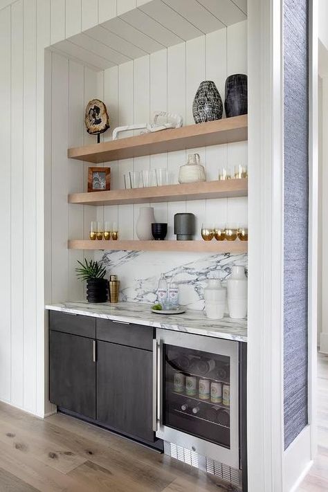 Well-appointed bar nook is fitted with floating blond wood shelves stacked against a white shiplap backsplash over black cabinets and a glass front beverage fridge fixed beneath a black and white marble countertop fitted against a black and white marble backsplash. Small Home Bar Ideas, Small Wet Bar, Black Bar Cabinet, Wine And Coffee Bar, Small Bars For Home, Bar Nook, Home Wet Bar, Home Bar Rooms, Coffee Bar Design