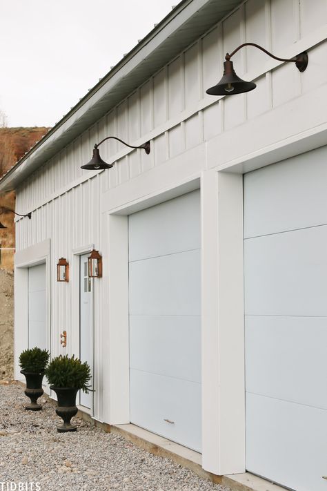 Garage Curb Appeal Design Ideas. It was time to add some garage curb appeal to our new pole barn home. In this process post, we've added our steel siding, steel roofing, painted our garage doors, added light fixtures and more. Let me show you! #garagedesign #garage #curbappeal #garagecurbappeal #camitidbits #homeexterior #steelsiding #steelroofing White Garage, Metal Garage Ideas, White Metal Garage, Metal Garage, Barn Lights Exterior Garage, Garage Doors Farmhouse White, Garage Door Lightinf, Large Barn Lights Exterior Garage, Craftsman Style Garage Doors