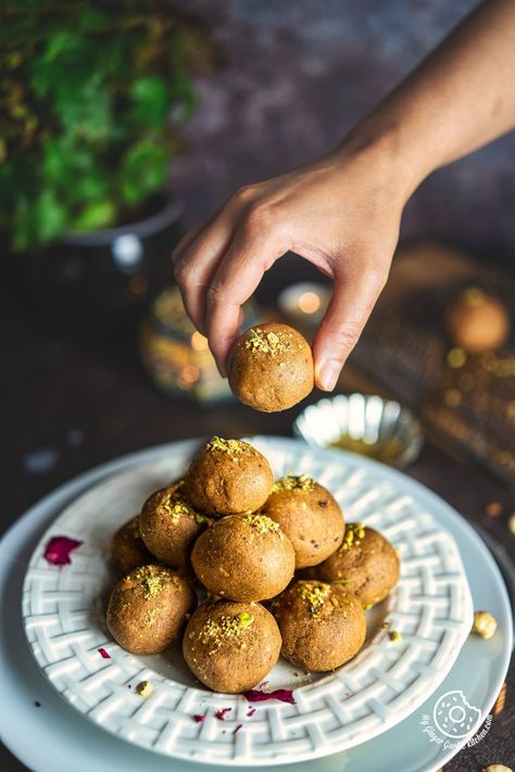 a hand picking one atta ladoo from the white plate stacked with atta ladoos Indian Sweet Photography, Laddoo Photography, Aliv Ladoo Recipe, Motichoor Ladoo Photography, Different Types Of Laddus, How To Make Motichoor Ladoo, Making Sweets, Making Ghee, Cafe Menu Design