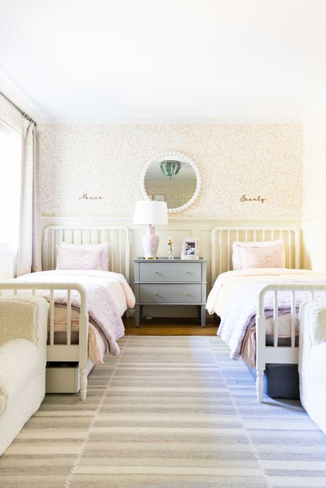 A girl's bedroom is her palace, ready to take on the world with style and comfort. This lovely girl's bedroom features two individual beds, a beautiful white and pink wall print, a round-shaped mirror, and a cute table lamp. Could it be any more charming Double Bed Girls Room, Twin Bed Girls Room, Bed Rug Placement, White And Pink Wall, Traditional House Decor, Pink Wall Print, Twin Girl Bedrooms, Girl Bedroom Ideas, Shared Girls Bedroom