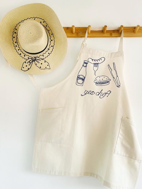 Upgrade your cooking and entertaining with our stylish embroidered apron, crafted from eco-friendly regenerated denim. Available in Indigo denim or Natural, it features two slanted side pockets with contrast trim and an adjustable knotted neckband for the perfect fit. Perfect for BBQs, kitchen adventures, and entertaining in style. Embroidery On Apron, Aprons Aesthetic, Apron Embroidery, Homemade Aprons, Embroidery Aprons, Yes Chef, Denim Apron, Embroidered Apron, Sewing Aprons