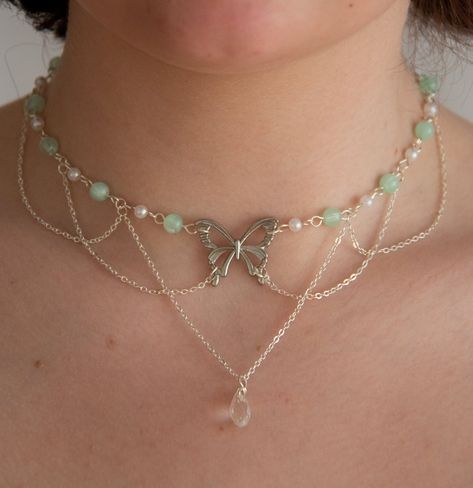 This necklace features delicate pastel green beads, lustrous pearls, and draped chains, creating a layered, fairy and ethereal look. In the heart of this necklace, a captivating butterfly pendant and a sparkling clear crystal pendant add a touch of timeless beauty.  The layers of draped chains add depth and dimension to the necklace, allowing it to rest gracefully against your neckline, accentuating your natural beauty. The delicate nature of this piece ensures it is suitable for any occasion, from casual outings to formal events, making it a versatile addition to your jewellery collection. Elevate your style with this exquisite accessory, effortlessly blending sophistication with a touch of enchantment.  The pastel green beads interspersed between the pearls create a harmonious colour pal Beautiful Handmade Jewelry, How To Make A Layered Necklace, Fairy Crystal Necklace, Ideas For Necklaces With Beads, Ethereal Jewelry Necklaces, Fairy Pearl Necklace, Purple Fairy Necklace, Crystal Handmade Jewelry, Crystal Necklaces Ideas