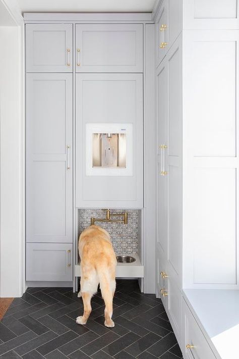 Black herringbone mudroom floor tiles lead to built-in dog food bowls fixed beneath a brass swing arm pot filler fixed to white and blue mosaic wall tiles under a water dispenser. Dog Food Cabinet, Mudroom Dog Room, Dog Food Area, Dog Nook, Dog Cabinet, Dog Food Station, Mudroom Flooring, Dog Feeding Station, Dog Storage