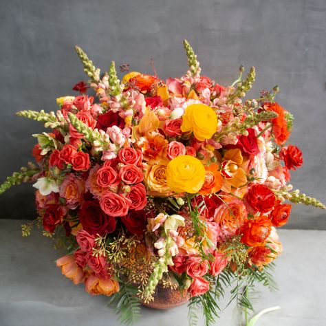 This dual-toned arrangement is ablaze with a gradient of colors, featuring a lush and vibrant bouquet a-top an exquisite underwater scene. The fiery orange tones of spray roses, free spirit roses, shimmer roses, and red roses are complemented by the warmth of orange tulips and cymbidium orchids. The addition of red butterfly ranunculus, yellow ranunculus, and snapdragons adds an extra burst of color, while the seeded eucalyptus and winter roses provide a perfect green contrast. The stunning vase Tall Bouquet Centerpiece, Orange Floral Bouquet, Red Orange Yellow Flower Arrangement, Yellow And Red Flower Arrangements, Sunset Color Flower Arrangements, Artichoke Floral Arrangement, Red Orange Yellow Flowers, Red Roses Flower Arrangement, Ranaculus Wedding Bouquet