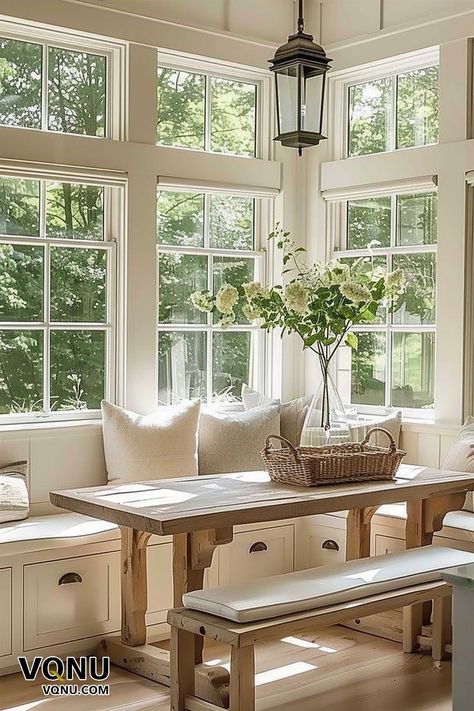 A bright breakfast nook featuring large windows, a wooden table with benches, soft cushions, and fresh flowers in a vase, creating a serene and airy atmosphere. Benches Under Windows, Window Nook Ideas Kitchen, Window Seat Dining Table, Conservatory Inspiration, Simple Wooden Table, Beautiful Houses Exterior, Creative Bathroom Design, Neutral Bedroom Design, Sunroom Dining